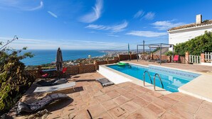 Une piscine sur le toit avec vue sur l’océan, des espaces de détente en plein air et un ciel dégagé.