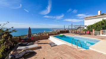 A rooftop pool with a view of the ocean, outdoor seating, and a clear sky.