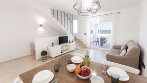 A modern living room with a staircase, a dining area with a table set for two, and a sofa. - Vistamar 1 in Oliva With 2 Bedrooms and 1 Bathrooms (Oliva)