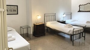 A room with three beds, a wooden nightstand with a lamp, a small table, and a framed picture on the wall. - Cavour 36 in Firenze (Florence)