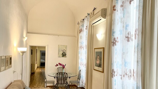 A cozy living room with a sofa, a small round table, and chairs. There is a painting on the wall and an air conditioning unit above the table. - Cavour 36 in Firenze (Florence)