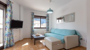 A living room with a sofa, a coffee table, a flat-screen TV, and a window with curtains. - Tolox 1 in Tolox With 1 Bedrooms and 1 Bathrooms (Tolox)