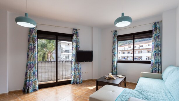 A modern living room with a sofa, a TV, and a balcony with patterned curtains. - Tolox 1 in Tolox With 1 Bedrooms and 1 Bathrooms (Tolox)