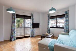 A modern living room with a sofa, a TV, and a balcony with patterned curtains. - Tolox 1 in Tolox With 1 Bedrooms and 1 Bathrooms (Tolox)