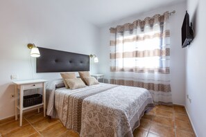 Ein Schlafzimmer mit einem großen Bett, zwei Nachttischen, einem an der Wand befestigten Fernseher und einem Fenster mit gemusterten Vorhängen.