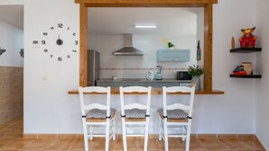 A kitchen with a wooden counter, three white chairs, a clock, and a microwave. - Tolox 1 in Tolox With 1 Bedrooms and 1 Bathrooms (Tolox)