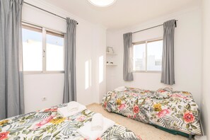 Quarto com duas camas, cortinas cinzentas e uma janela.
