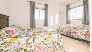 Un dormitorio con dos camas, cortinas grises, una lámpara de techo blanca y un ventanal con vistas al exterior.