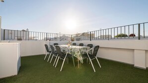 Una terraza en la azotea con mesa y sillas, rodeada por una barandilla metálica, y vistas de la ciudad.