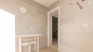 Un baño moderno con azulejos color beige, un lavamanos blanco y una pequeña mesa con dos taburetes.