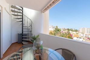 A balcony with a glass table, wicker chairs, a potted plant, and a spiral staircase. - Yucas Vistamar in Fuengirola (Fuengirola)
