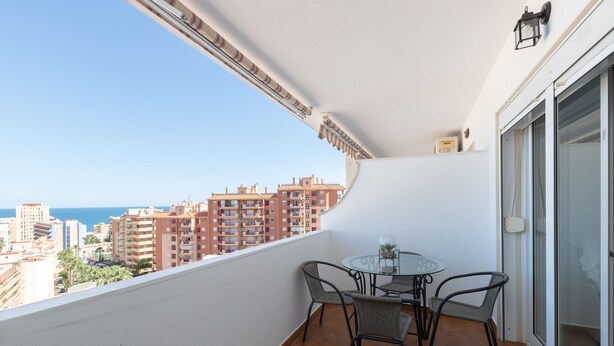 A balcony with a glass table and chairs, a potted plant, and a view of buildings and the sea. - Yucas Vistamar in Fuengirola (Fuengirola)