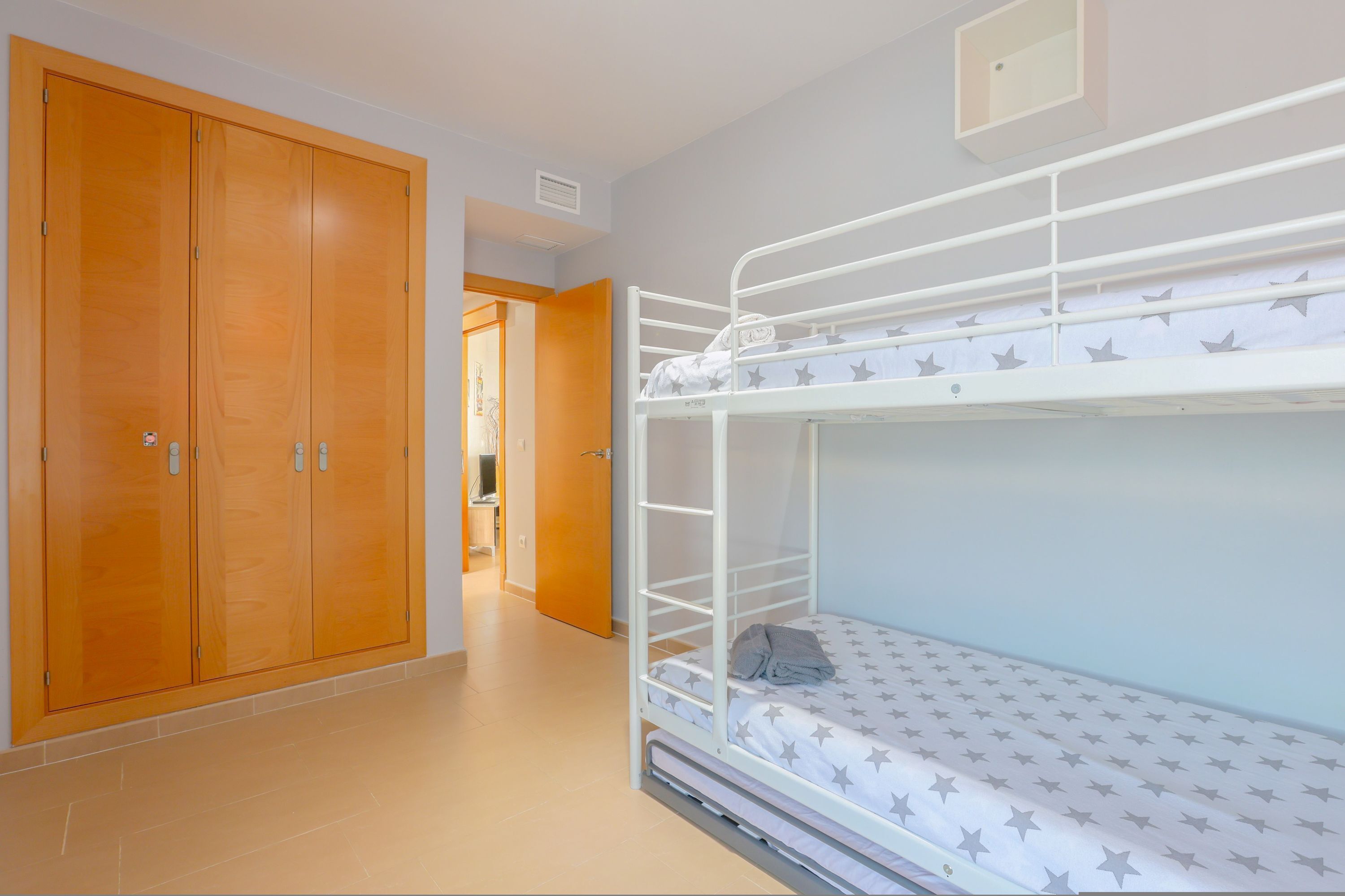 Un letto a castello con materasso a motivi stellati, un'armadietto in legno e un corridoio che porta a un'altra stanza.