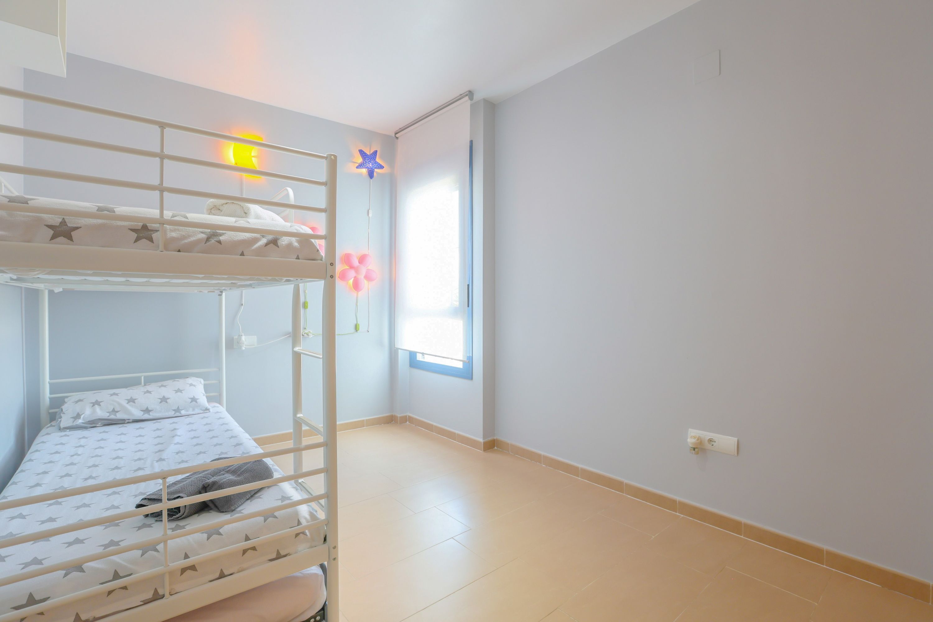 A bunk bed room with a star-patterned bedspread, a window with a view, and a wall socket.