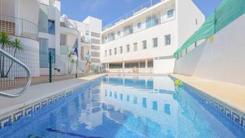 A swimming pool with a tiled edge, surrounded by white buildings with balconies and a clear blue sky.