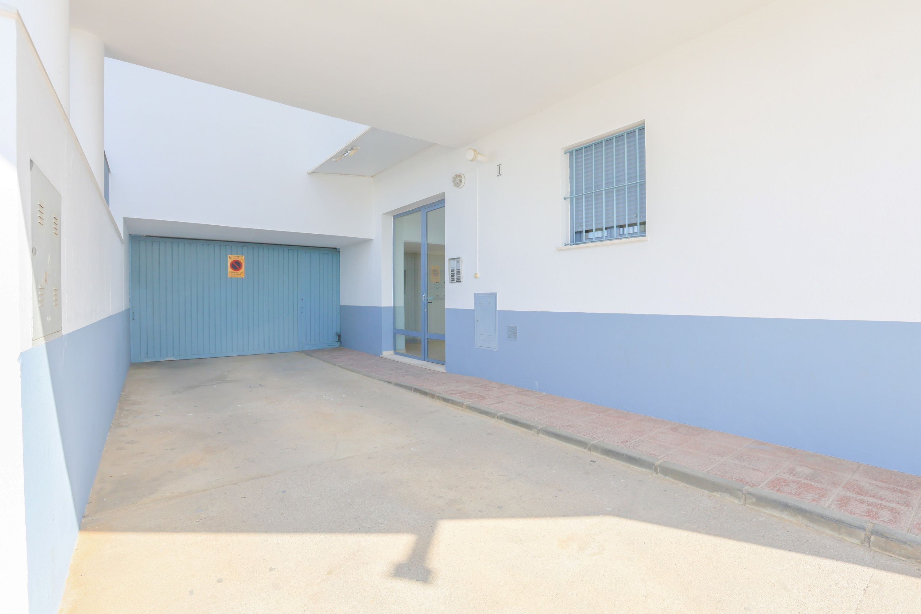 Ein Gebäude mit blauer und weißer Fassade, einer Garagentür, einer Tür mit Glasfenster und einem kleinen, vergitterten Fenster.