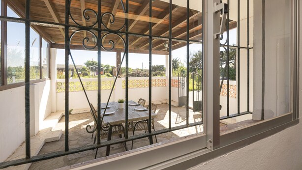 Un patio cubierto con mesa y sillas, barandilla y vistas del paisaje circundante.