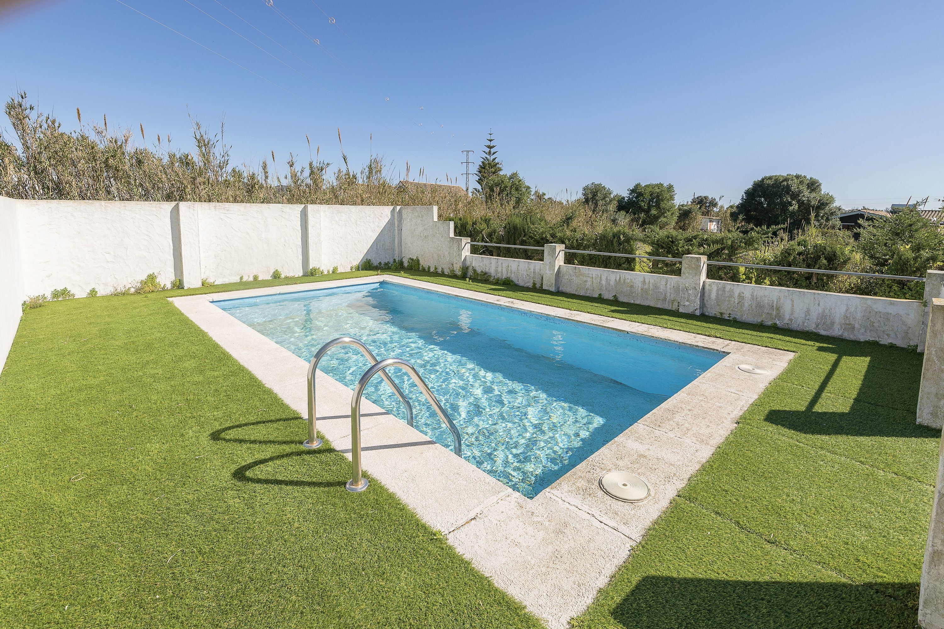 Una piscina rectangular con una escalera metálica, rodeada de césped artificial y bordes de hormigón.