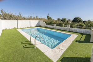 Una piscina rectangular con una escalera metálica, rodeada de césped artificial y bordes de hormigón.