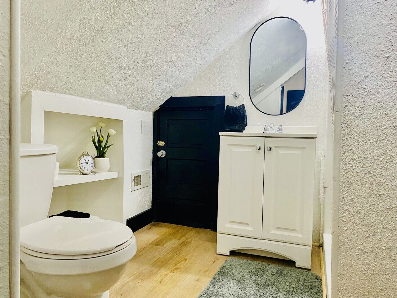 Une salle de bain avec des toilettes, un meuble blanc, un miroir et une porte.