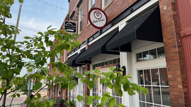 A brick building with a storefront for 'Red's Donuts' and a sign for 'West End Real Estate'. - Little Red Loft | Cozy Guest Suite Apartment (Danville)