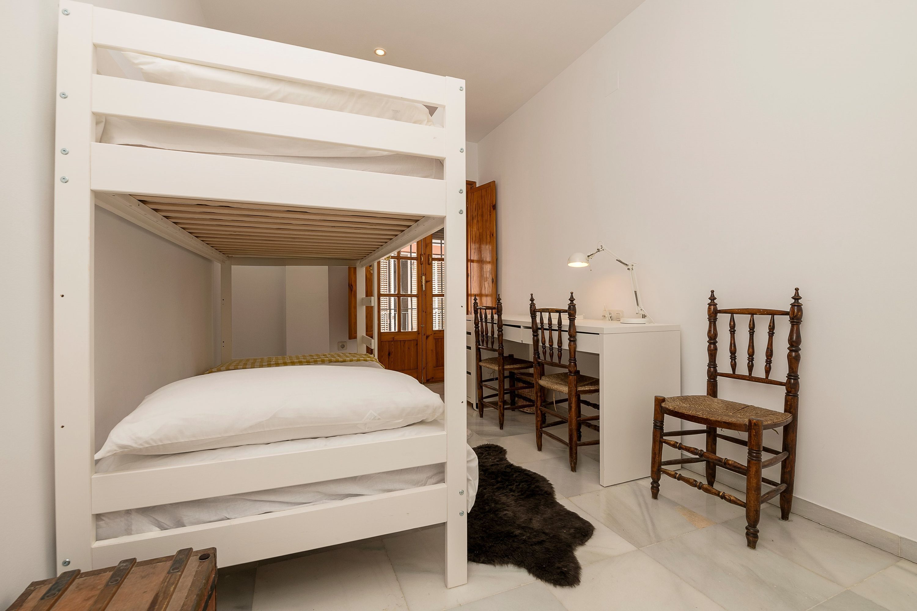Un lit superposé avec une tête de lit en bois, un bureau avec une chaise et une lampe.