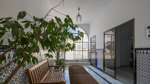 Un couloir avec un banc en bois, un mur carrelé et une vue à travers une porte vitrée.