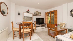 Un salon comprenant une table à manger, des chaises, un téléviseur, un meuble en bois et une grande fenêtre.