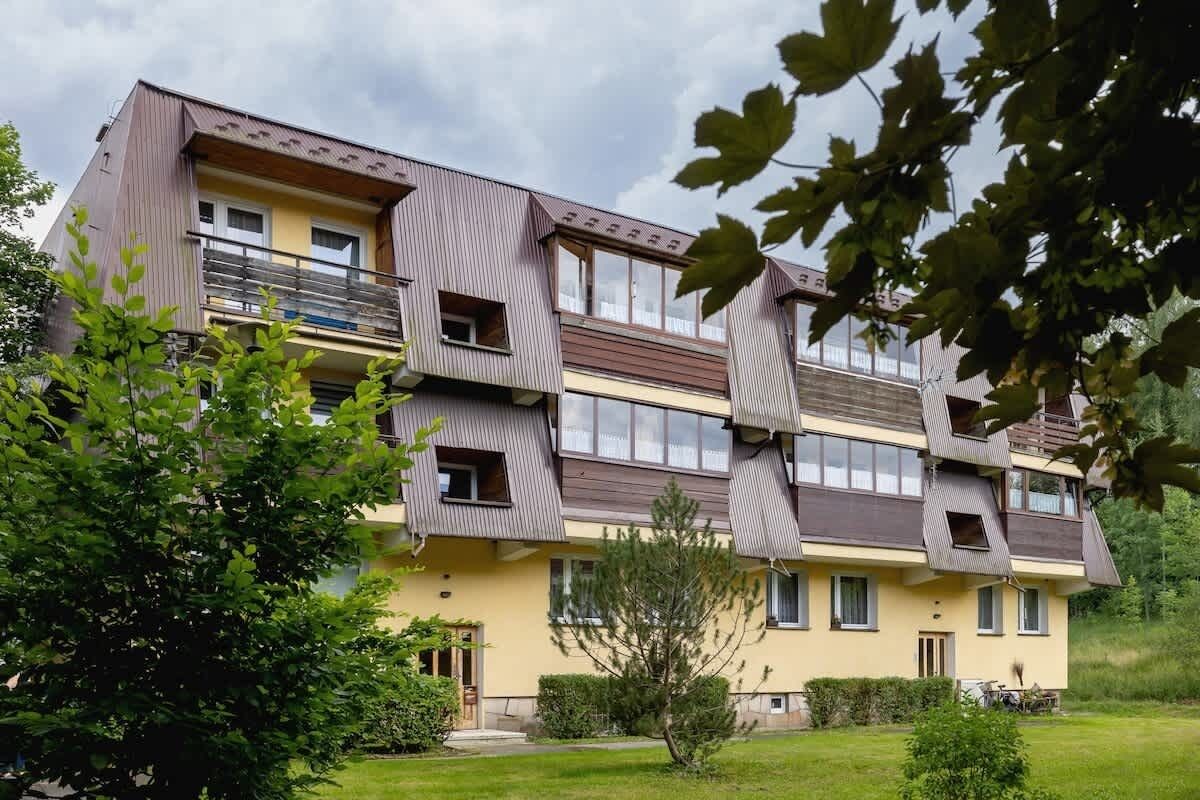 A multi-story residential building with balconies, a garden, and a clear sky.