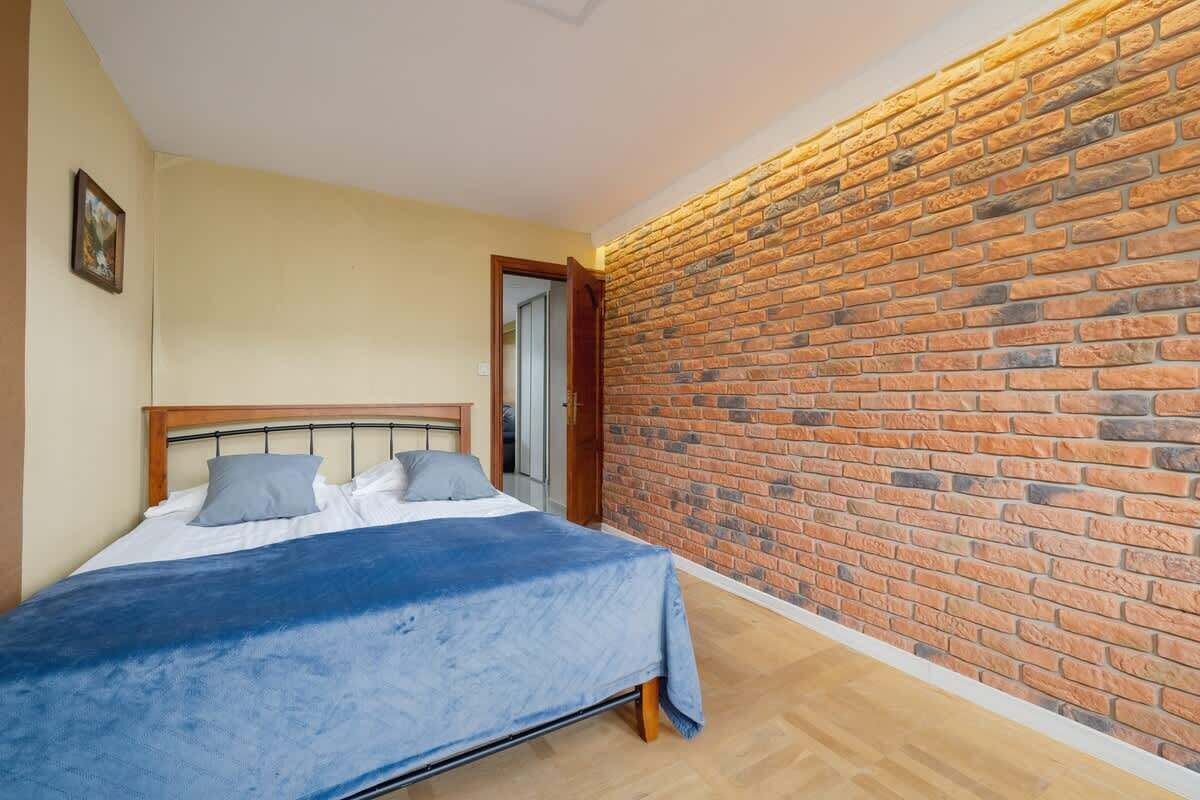 Ein Schlafzimmer mit Backsteinwand, einem Bett mit blauer Bettdecke und einem hölzernen Kopfteil.