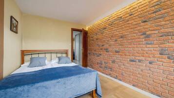 A bedroom with a brick wall, a bed with a blue bedspread, and a wooden headboard.