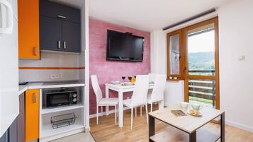 A compact kitchen with a microwave, a dining table with chairs, and a TV mounted on the wall.