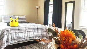 A bedroom with a bed, pillows, a lamp, a mirror, and a window with curtains.