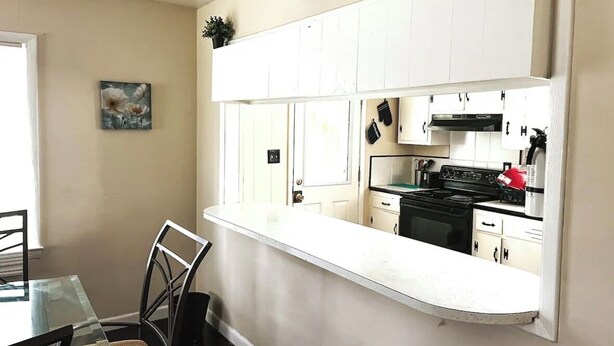A compact kitchen with white cabinets, a black stove, and a small dining area with a glass table and chairs.