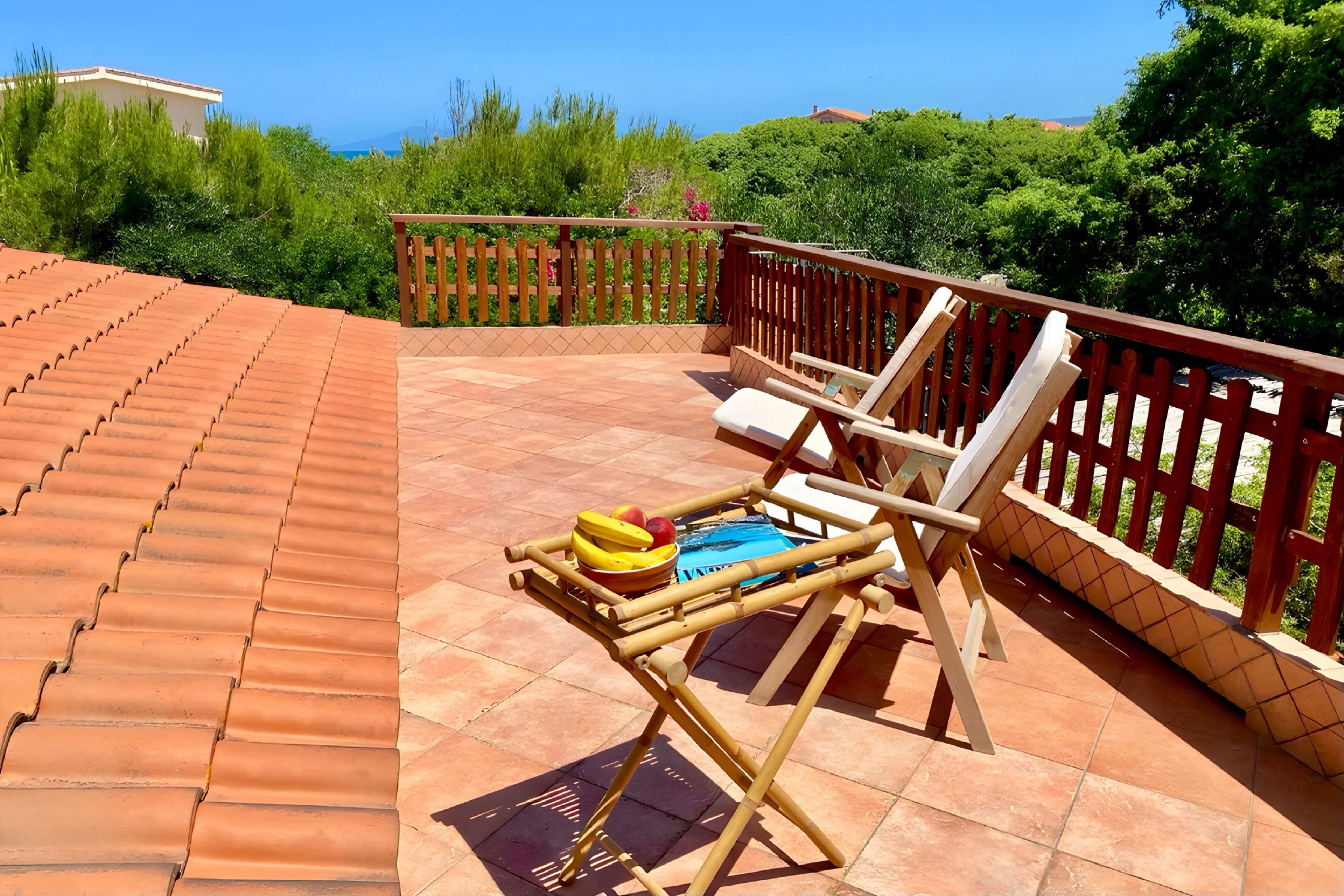 Eine Terrasse mit Terrakottafliesen, einem Holzzaun und einem Tisch mit Früchten und einem Kissen.