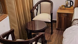 Hotelkamer met houten vloer, een bed met wit beddengoed, twee houten stoelen, een klein rond tafeltje, een nachtkastje met waterkoker en een wandlamp.