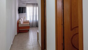 A hallway with a wooden door, a ceiling light, and a sofa in the background. - Hotel Horizon Ksamil (Ksamil)