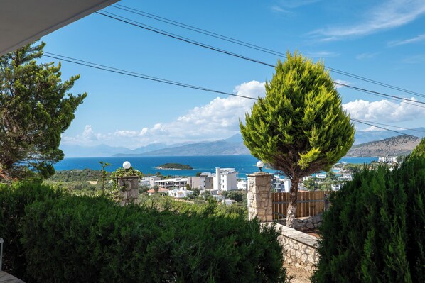 A coastal view with a stone wall, a tree, and buildings in the background. - Hotel Horizon Ksamil (Ksamil)