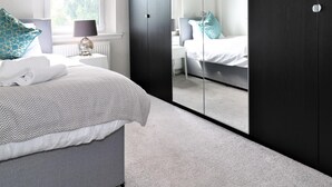 Ein Schlafzimmer mit Bett, Nachttisch, Lampe und einem großen Spiegel.