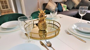 Ein Esstisch ist mit weißen Tellern, goldartigem Besteck und einer Ananas als Mittelstück gedeckt.