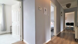 Ein Flur mit einer hellgrauen Wand, einer weißen Tür und einem Thermostat an der Wand.