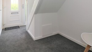 A clean, white interior with a staircase leading to an upper floor, a door with a window, and a small table. - Troon House - East Kilbride (Glasgow)