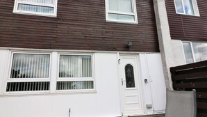 A two-story residential building with a white door and windows, a small porch, and a glass table with chairs. - Troon House - East Kilbride (Glasgow)