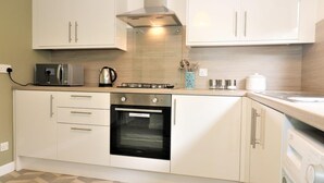 A compact kitchen with white cabinets, a built-in oven, a microwave, and a washing machine. - Troon House - East Kilbride (Glasgow)