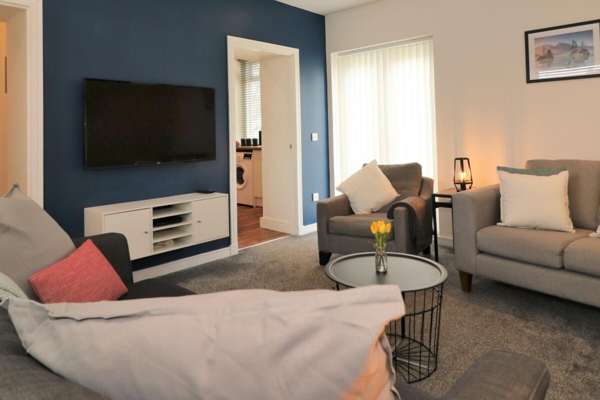 A modern living room with a flat-screen TV, grey sofas, a coffee table with a vase, and a painting on the wall.