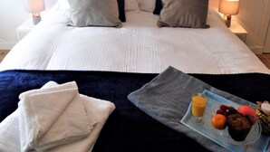 A neatly made bed with pillows, a bedside table with a lamp, and a tray with fruit and juice. - Stanefield House Motherwell (Motherwell)
