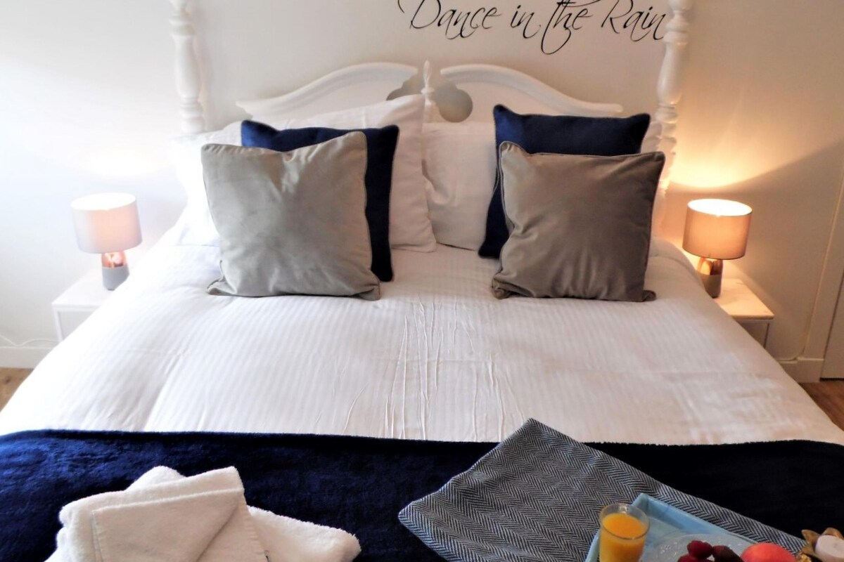 A neatly made bed with pillows, a bedside table with a lamp, and a tray with fruit and juice.