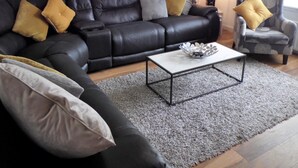 A living room with a black leather sofa, a grey patterned wall, a grey rug, and a small table with a decorative bowl. - Stanefield House Motherwell (Motherwell)