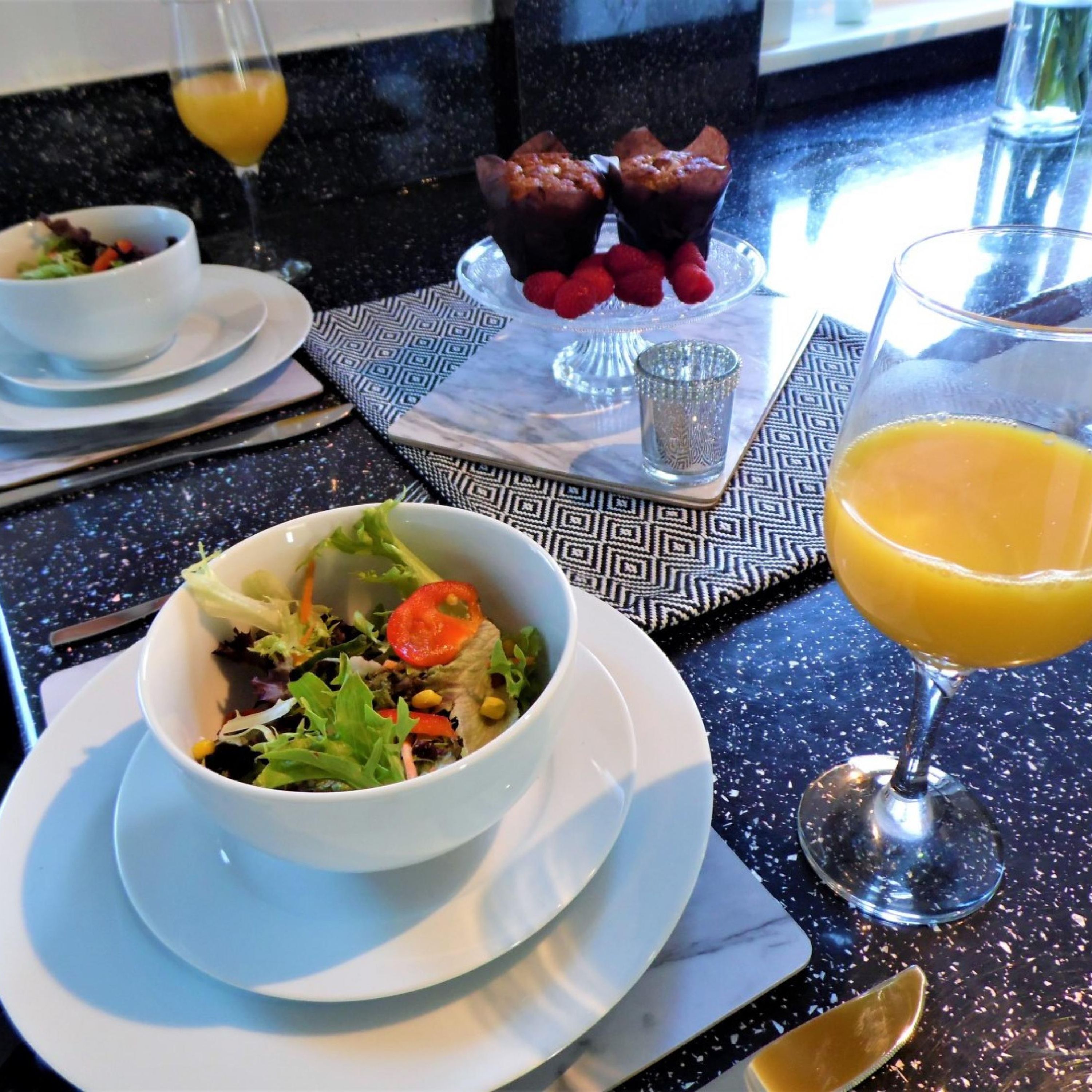 A breakfast setting with a salad, muffins, raspberries, and orange juice on a table.