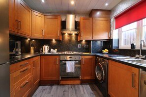 A modern kitchen with wooden cabinets, stainless steel appliances, and a red window blind. - Chapelhall House - Airdrie (Airdrie)